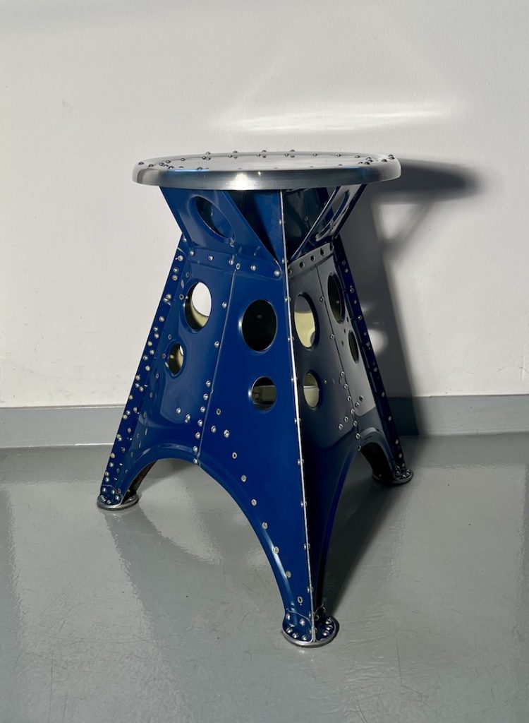 Das Projekt Aero 1946 kombiniert die Handwerksarbeit nach dem klassischen Flugzeugbau der 1940er Jahre mit dem Prinzip des Upcyclings. Das Material stammt in der Regel von Heckauslegern, Finne oder Elevatoren alter BELL-Hubschrauber. Die ultraleichten Hocker sind stylische Unikate und sehr belastbar. Die unterschiedlichen Farben, Beschriftungen und Nietlöcher verweisen auf die ursprüngliche Verwendung. Jeder Hocker ist auf der Unterseite mit dem passenden Typenschild versehen.