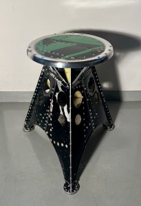 Das Projekt Aero 1946 kombiniert die Handwerksarbeit nach dem klassischen Flugzeugbau der 1940er Jahre mit dem Prinzip des Upcyclings. Das Material stammt in der Regel von Heckauslegern, Finne oder Elevatoren alter BELL-Hubschrauber. Die ultraleichten Hocker sind stylische Unikate und sehr belastbar. Die unterschiedlichen Farben, Beschriftungen und Nietlöcher verweisen auf die ursprüngliche Verwendung. Jeder Hocker ist auf der Unterseite mit dem passenden Typenschild versehen.